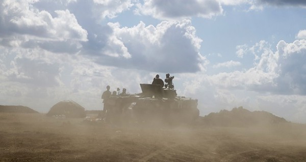 Ukrainian army servicemen around an armoured vehicle are seen through dust raised by passing vehicles near Debaltseve